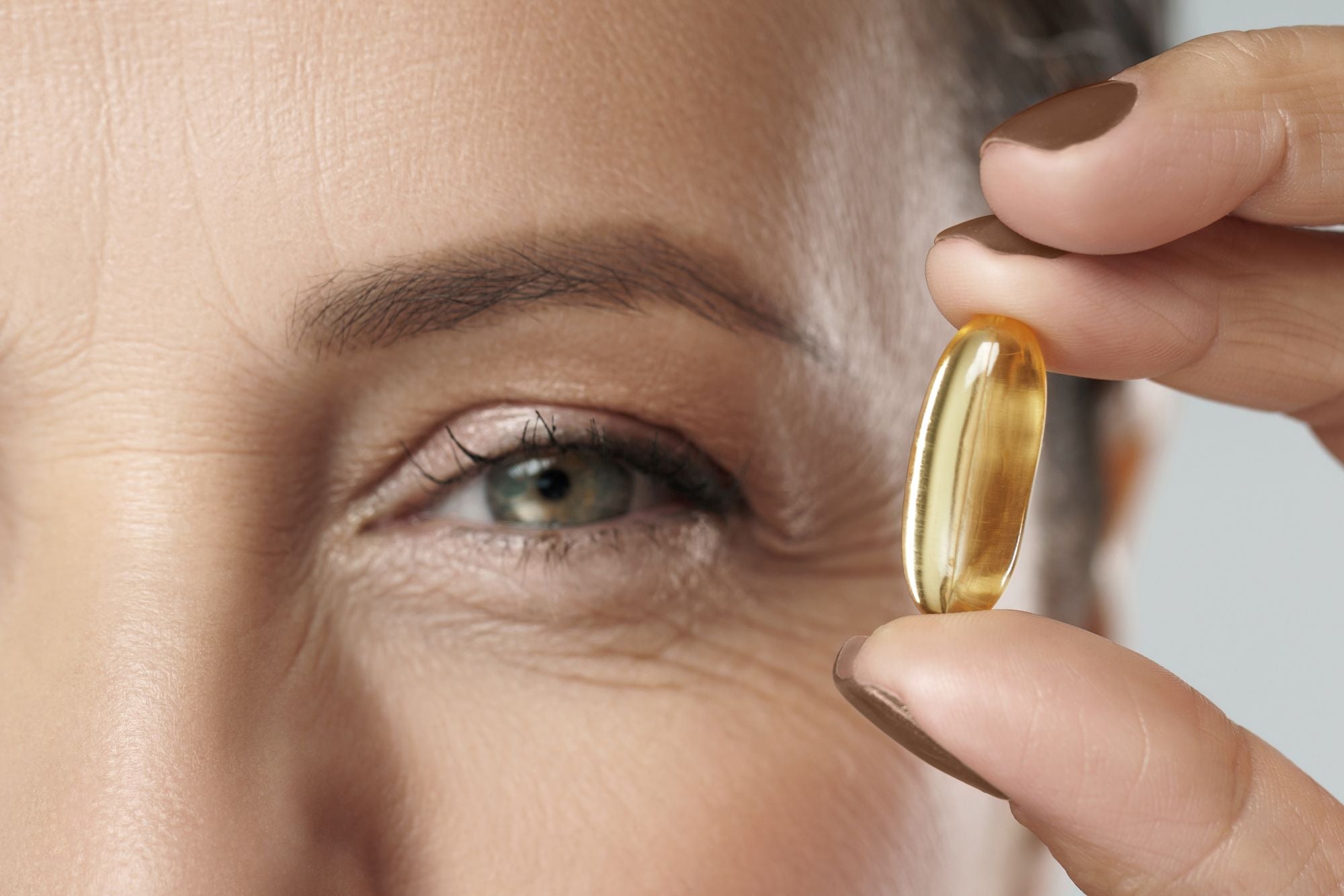 Frau, die sich eine Omega-3-Kapsel neben das Auge hält