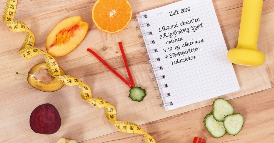 Ziele für 2026: Gesund ernähren, regelmäßig Sport machen, 10 kg abnehmen, Stress reduzieren – Notizbuch mit Obst, Maßband und Hantel auf einem Holztisch