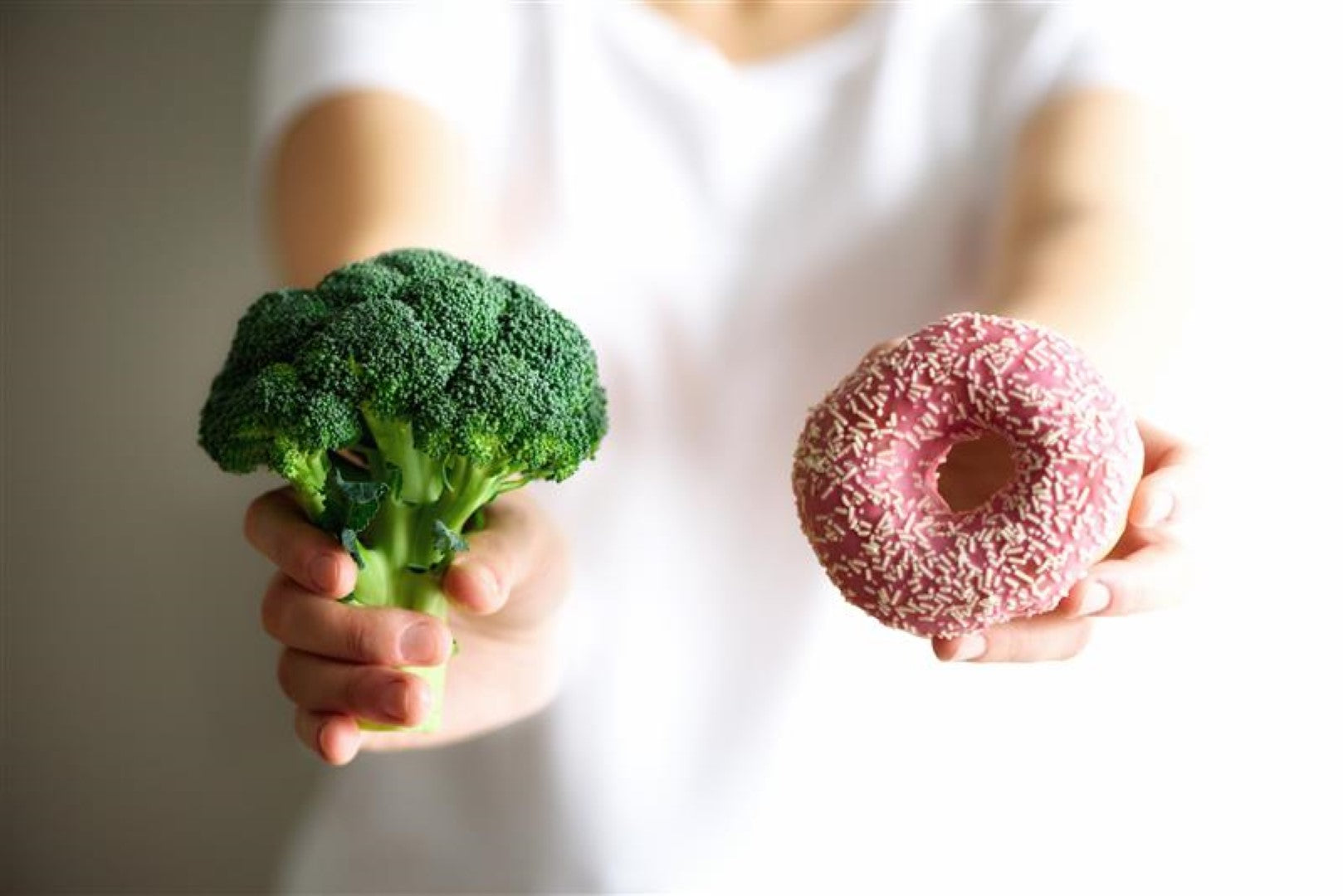 Die Person hält in einer Hand Brokkoli und in der anderen einen bunten Donut