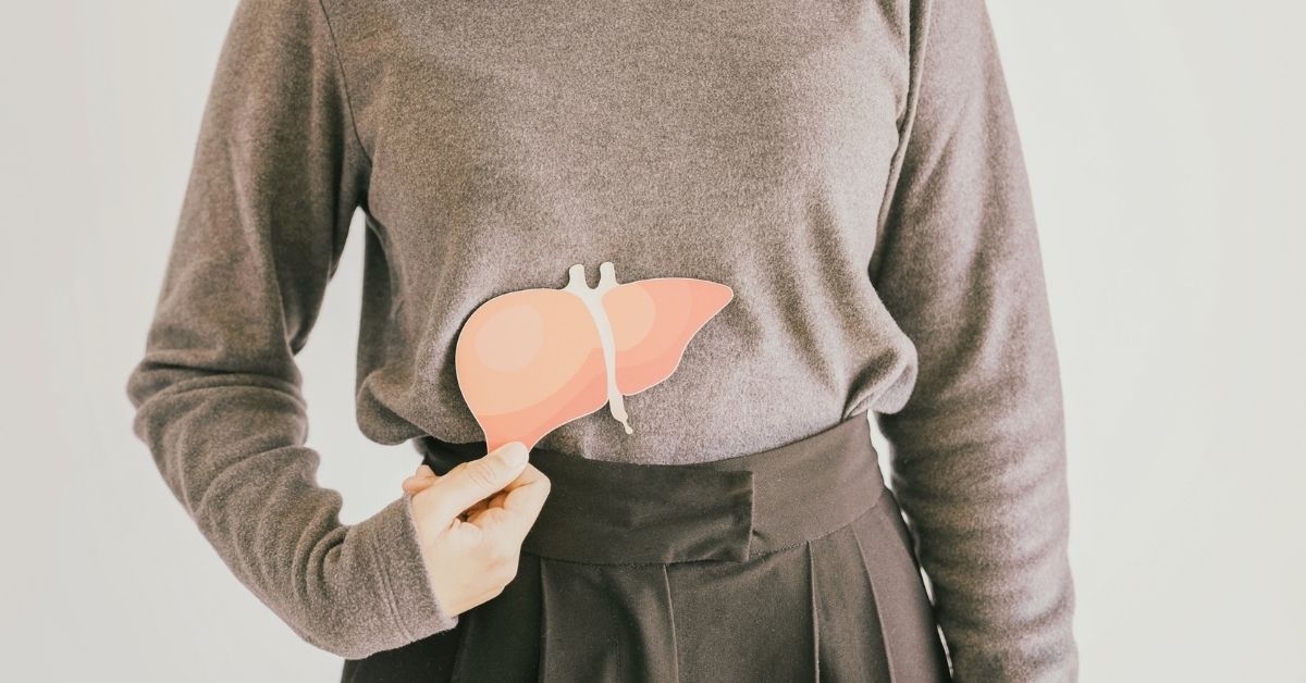 Frau hält eine Leberillustration vor den rechten Oberbauch als Symbol für Lebergesundheit und eine mögliche Fettleber.