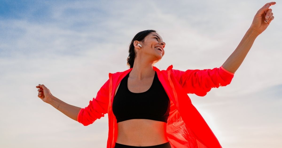 Sportliche Frau in roter Jacke streckt die Arme aus – Gesunde Leber ermöglicht ein gutes Wohlbefinden.