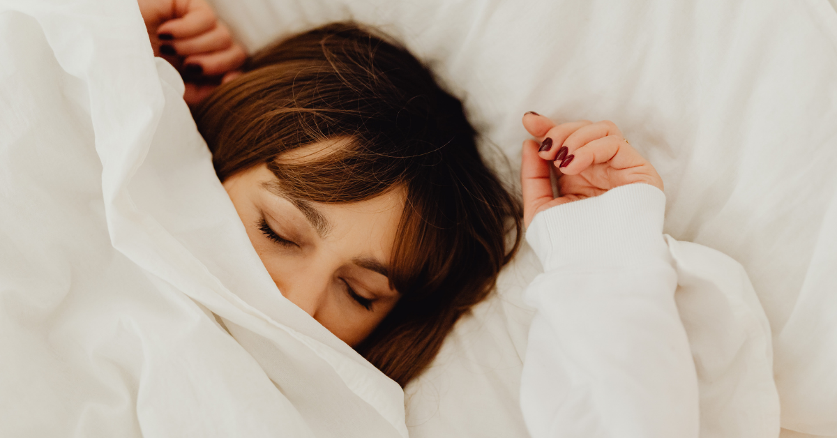 Schlafende Frau liegt entspannt mit geschlossenen Augen unter einer weißen Bettdecke – Melatonin Dosierung für besseren Schlaf.