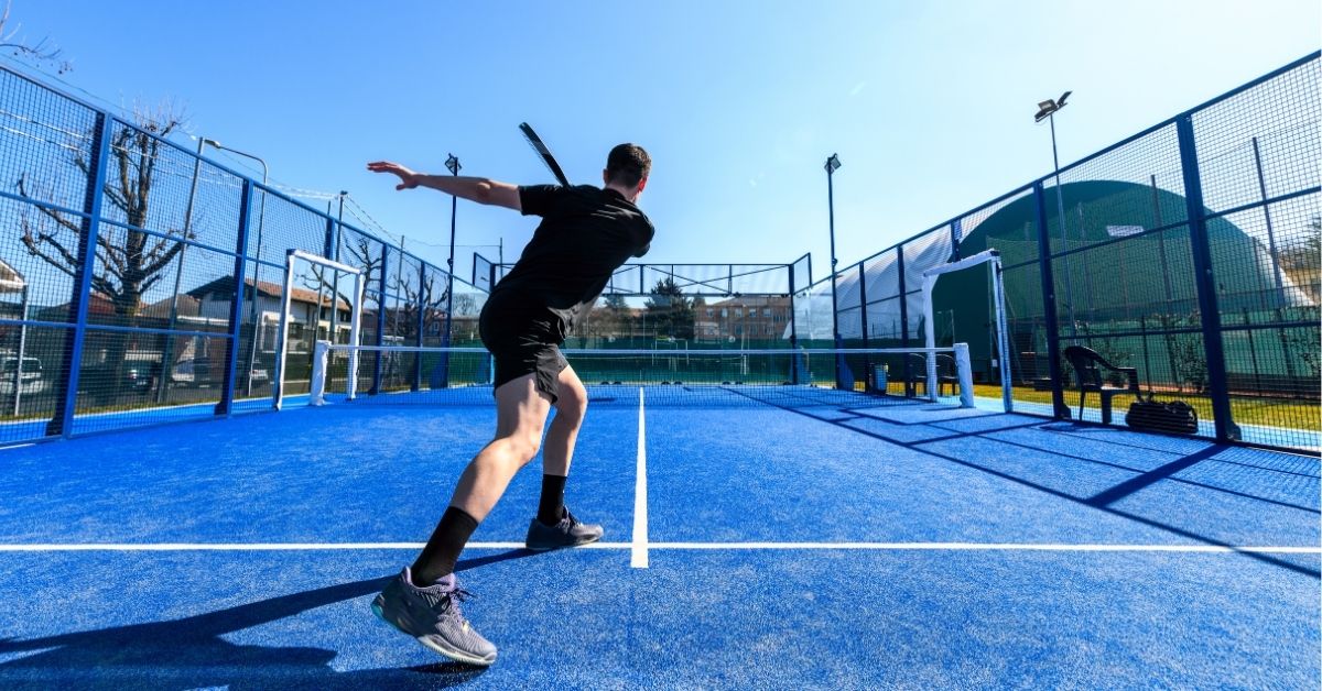 Padel-Spieler schlägt den Ball mit einem Padel-Schläger über das Netz auf einem sonnigen Court.