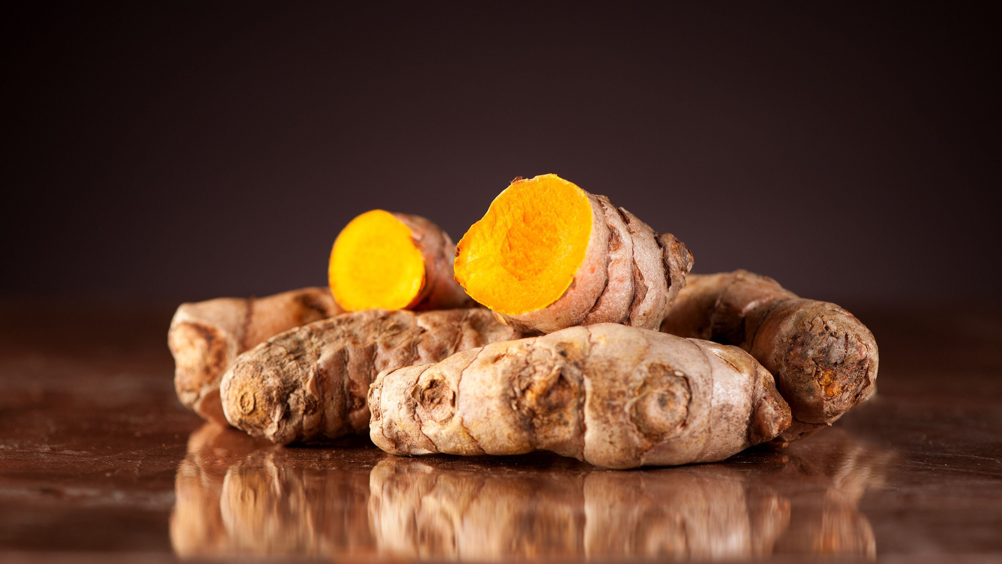 Nahaufnahme von frischer, halbierter Kurkumawurzel mit leuchtend orangem Inneren auf reflektierender Oberfläche