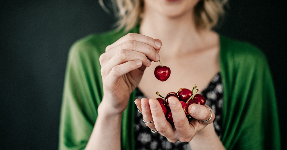 Frau hält Sauerkirschen in der Hand, Symbol für Sauerkirschen Nebenwirkungen