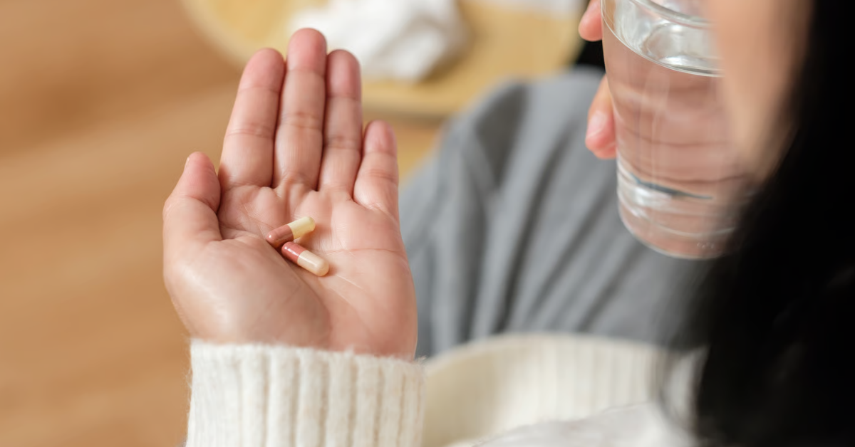 Person hält zwei Spermidinkapseln auf der Handfläche und ein Glas Wasser