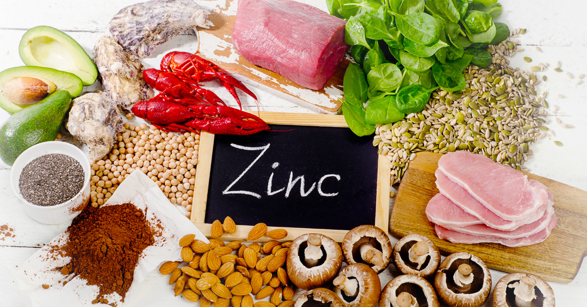 Zinkhaltige Lebensmittel wie Rindfleisch, Meeresfrüchte, Spinat, Kürbiskerne, Mandeln, Pilze und Hülsenfrüchte auf einem Tisch.