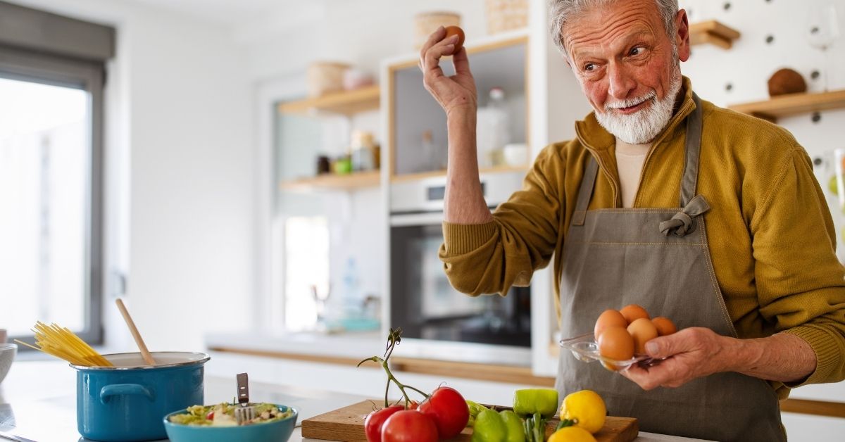 Älterer Mann bereitet in der Küche eine ausgewogene Mahlzeit mit frischen Zutaten zu – bewusste Ernährung bei Gicht