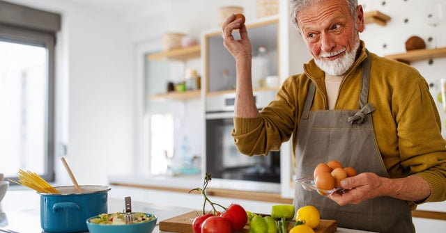 Älterer Mann bereitet in der Küche eine ausgewogene Mahlzeit mit frischen Zutaten zu – bewusste Ernährung bei Gicht