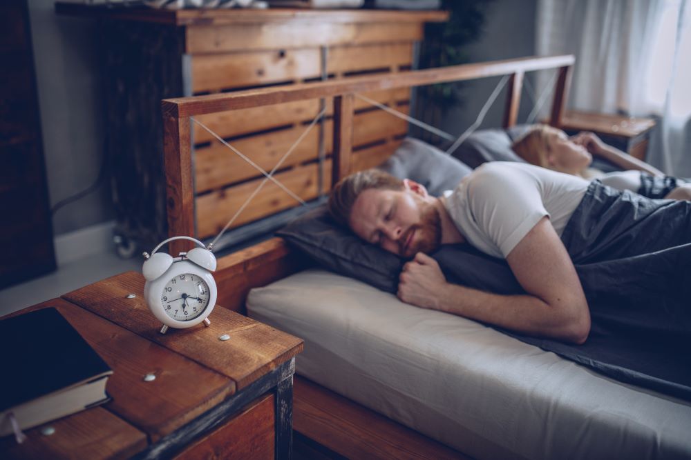Mann schläft und ein weißer Wecker steht auf dem Nachttisch