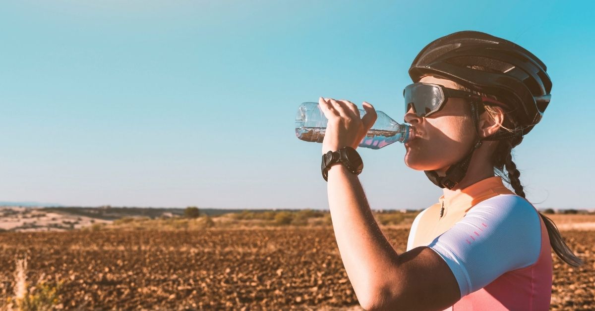 Radfahrerin trinkt während einer Radtour aus einer Wasserflasche und achtet auf ihre Flüssigkeitsversorgung beim Training.