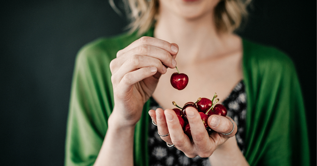 Frau hält Sauerkirschen in der Hand, Symbol für Sauerkirschen Nebenwirkungen