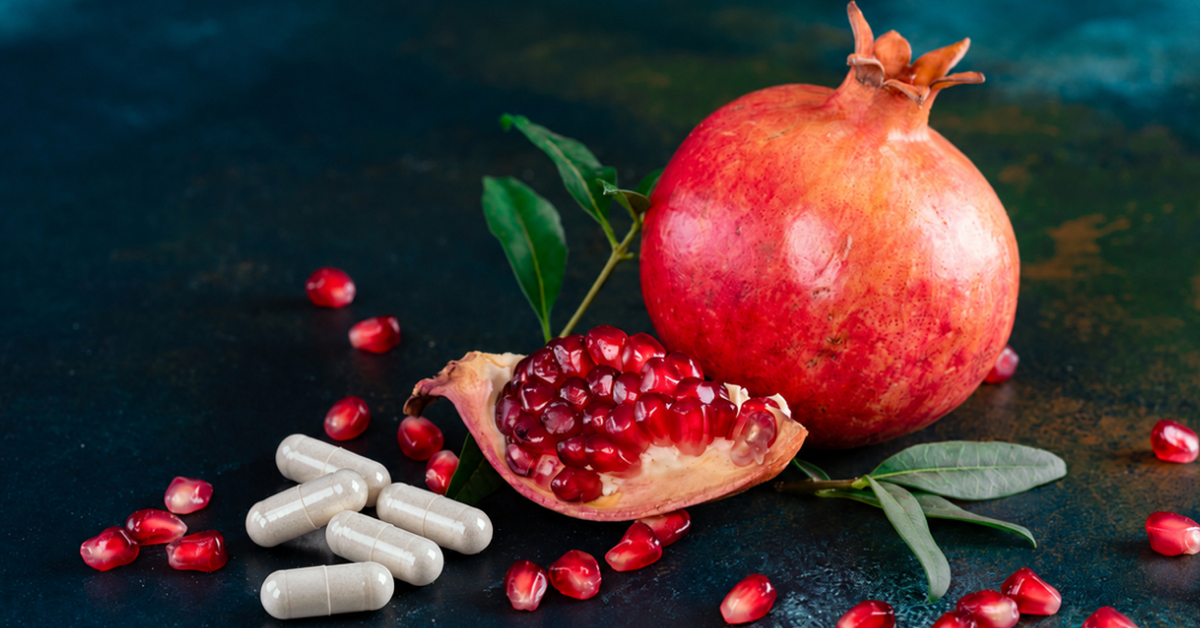 Granatapfel mit frischen Kernen und mehreren Kapseln auf dunklem Hintergrund zur Veranschaulichung der Urolithin A Dosierung.