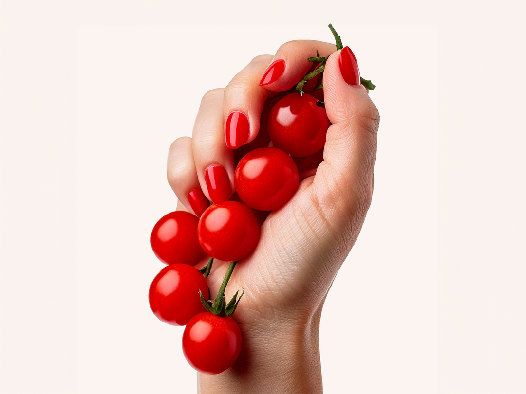 Hand mit rot lackierten Fingernägeln hält eine Rispe Cherrytomaten