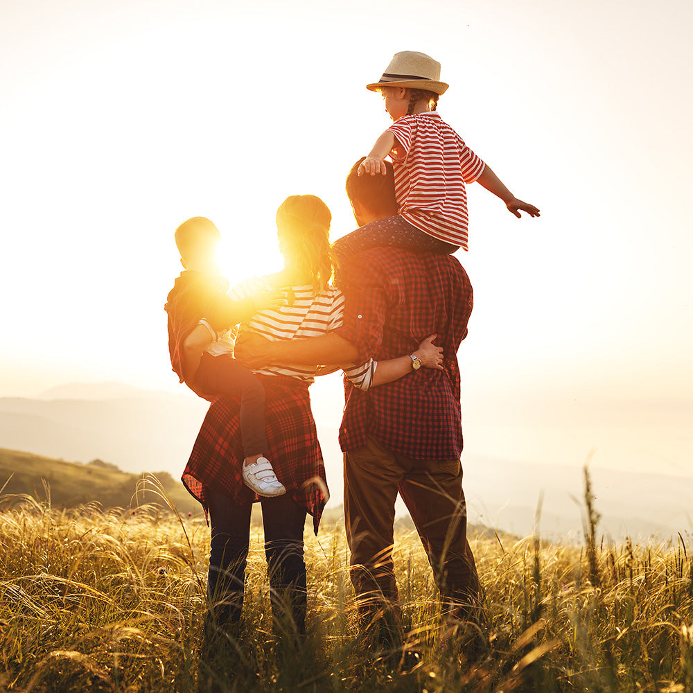 Familie mit zwei Kindern die auf einem Feld stehen und in den Sonnenuntergang schauen