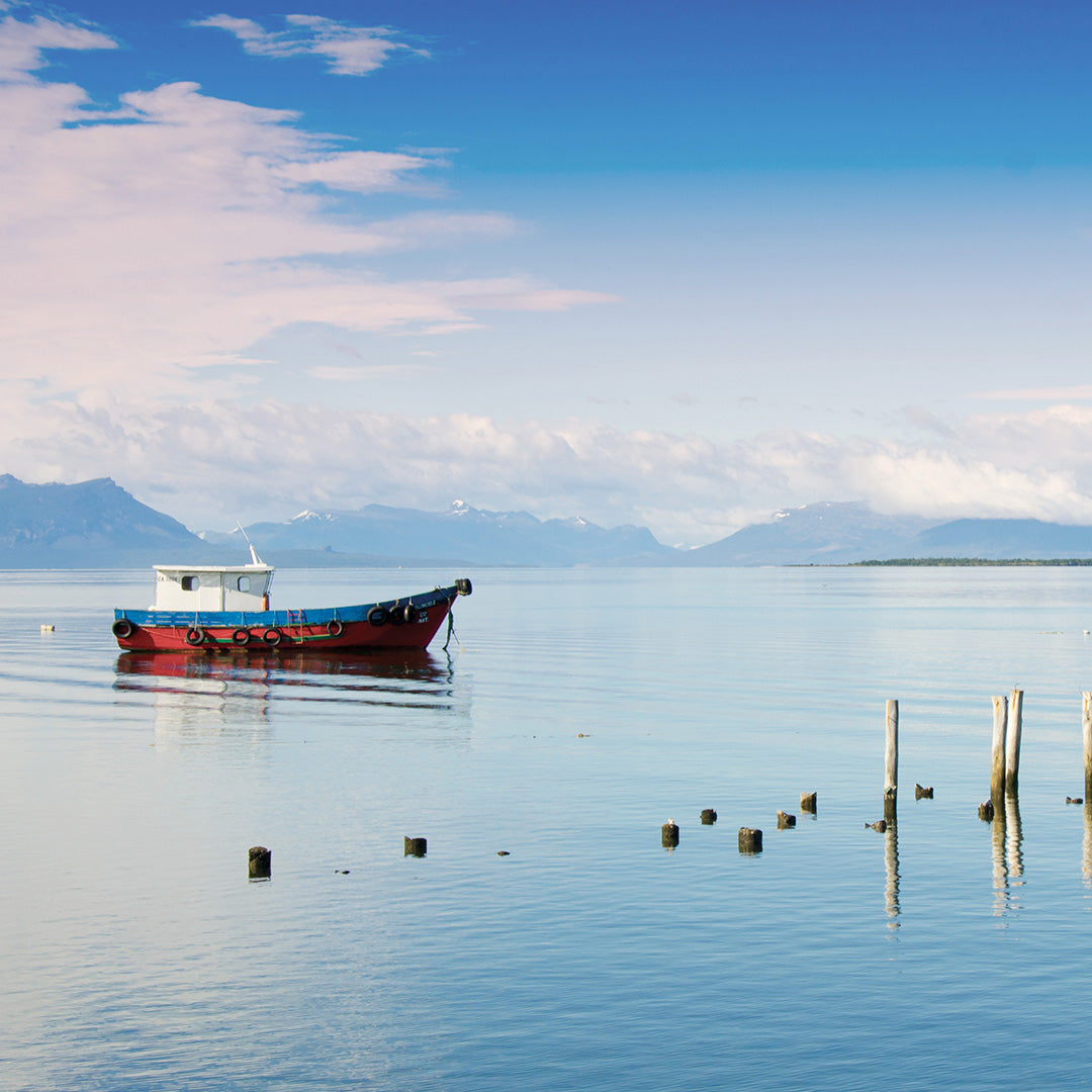 Fischerboot auf blauem Wasser mit Bergen und Wolken am Horizont